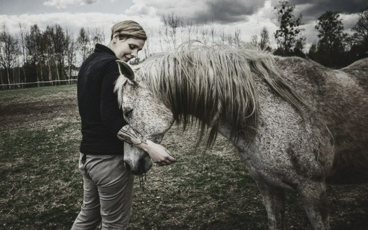 Kobieta przytulająca konia na pastwisku, w tle chmury.