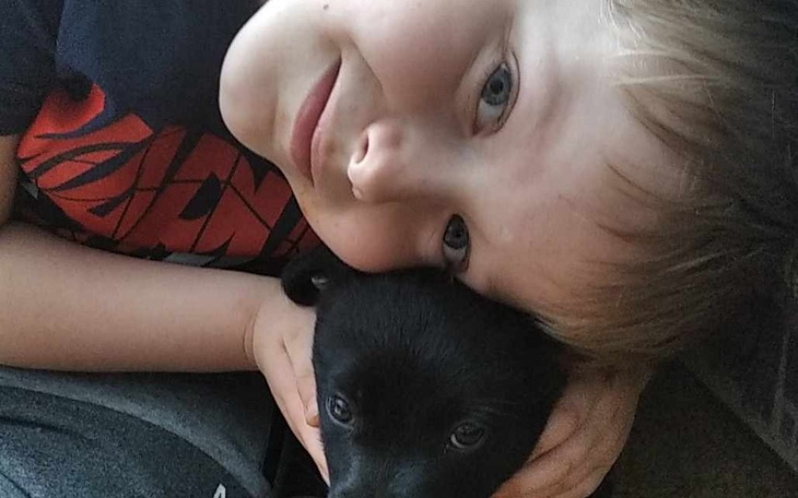 Chłopiec przytulający małego psa, oboje uśmiechnięci.