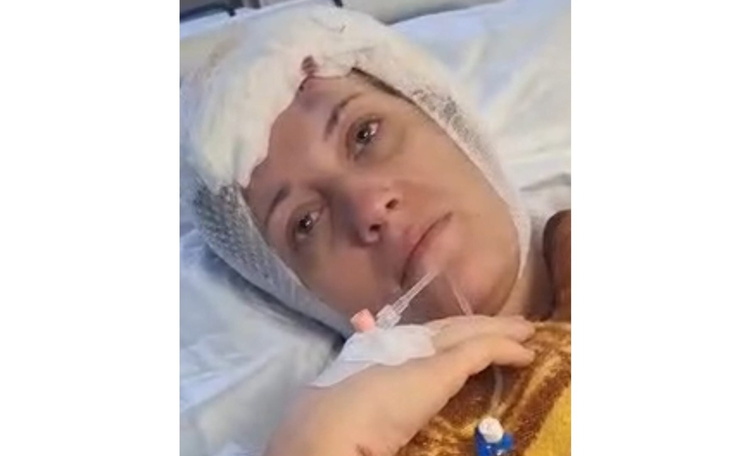 Kobieta w szpitalu, z opatrunkiem na głowie, wygląda na zmęczoną.