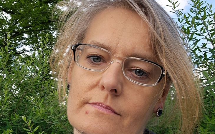 Kobieta z okularami, patrząca w stronę kamery w zielonym otoczeniu.