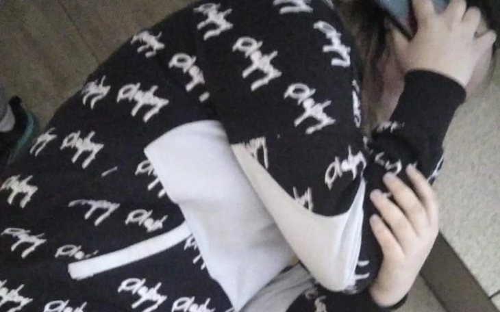 Osoba w czarnej bluzie, siedząca na podłodze, z telefonem.