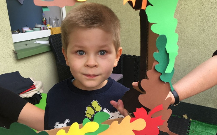 Chłopiec z uśmiechem, trzymający kolorową ramkę z papieru.