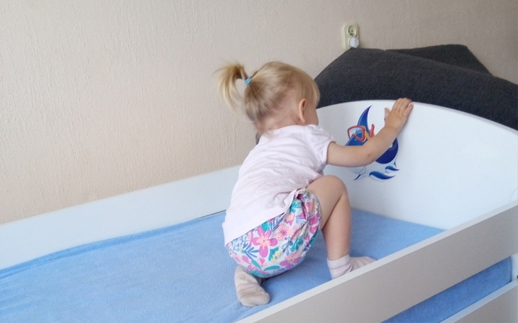 Mała dziewczynka wspinająca się na łóżko, bawiąc się przy tym.