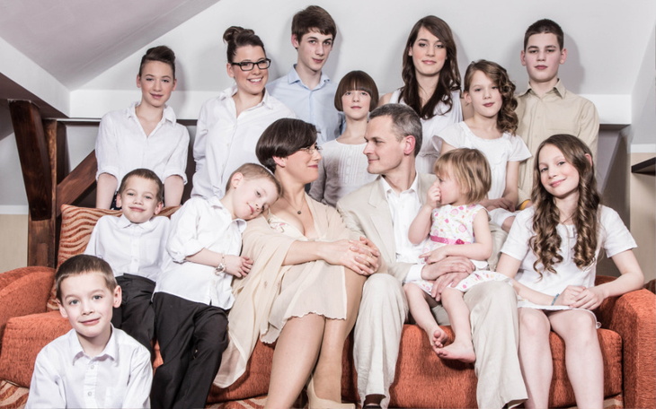 Rodzina pozująca na kanapie, wszyscy w białych i jasnych ubraniach.