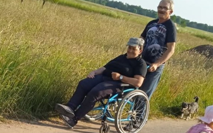 Mężczyzna pcha wózek inwalidzki po polu.