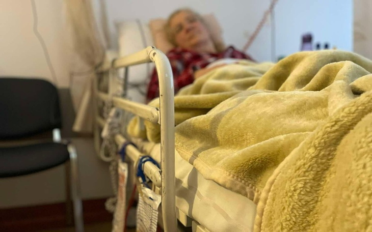 Osoba leżąca na łóżku szpitalnym, przykryta kocem.