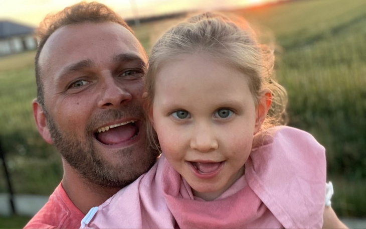 Uśmiechnięty tata z córką na tle zachodzącego słońca.