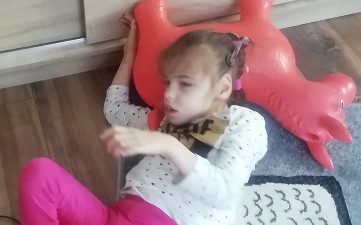 Dziewczynka leżąca na podłodze, z różowym balonem obok.