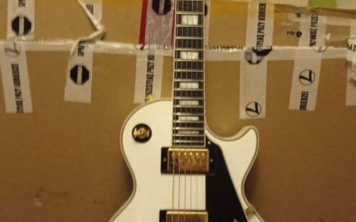 Biała gitara elektryczna na tle kartonu.