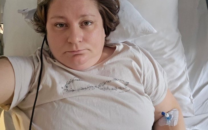 Kobieta leżąca w łóżku szpitalnym, z kroplówką i smutnym wyrazem twarzy.