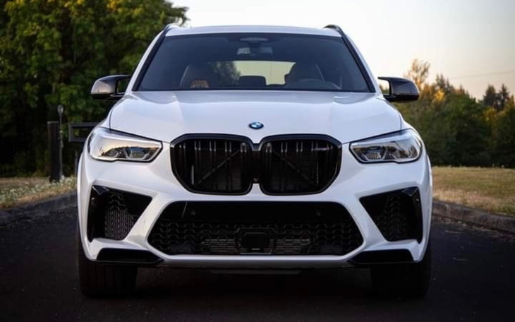 Biały samochód BMW X5 z przodu, na tle zieleni.