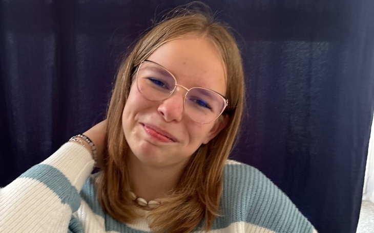 Młoda dziewczyna z okularami, uśmiechająca się do kamery.