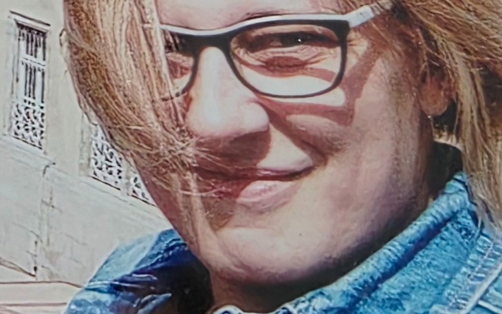 Portret osoby z okularami, uśmiechającej się na tle budynku.
