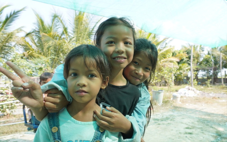 Trzy uśmiechnięte dziewczynki pozujące na tle palm.