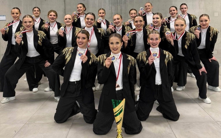 Zespół taneczny z medalami, uśmiechnięte tancerki w eleganckich strojach.