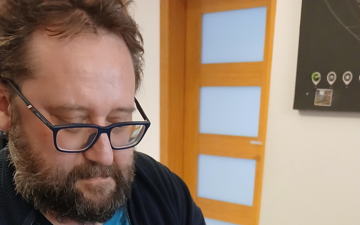 Mężczyzna z brodą, skupiony na zadaniu, w jasnym pomieszczeniu.