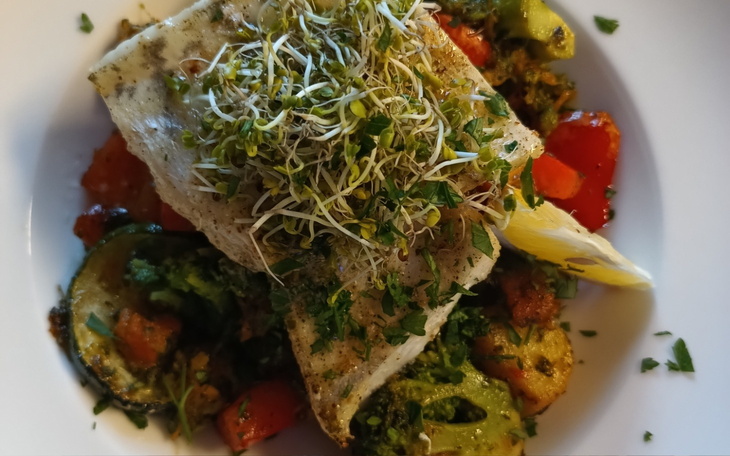 Danie z rybą i warzywami, udekorowane kiełkami.