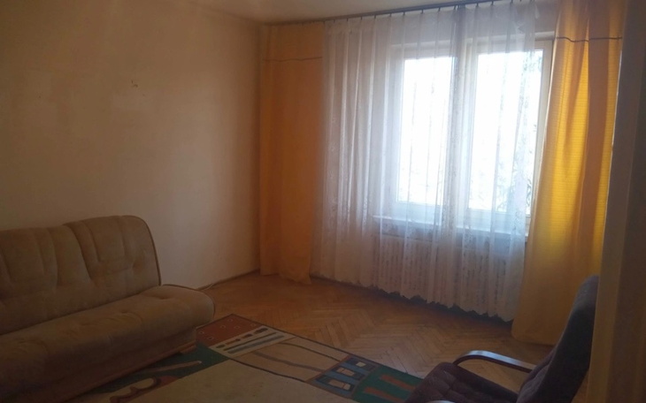 Pusty pokój z oknem i zasłonami, na podłodze dywan.