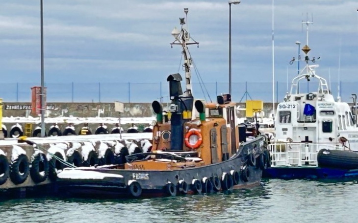 Tugboat w porcie, otoczony śniegiem i cumującymi łodziami.