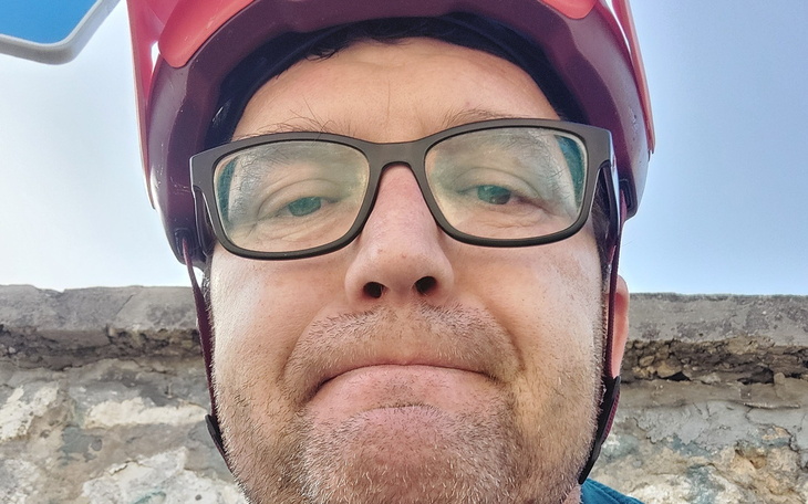 Mężczyzna w kasku rowerowym, patrzący w kamerę.