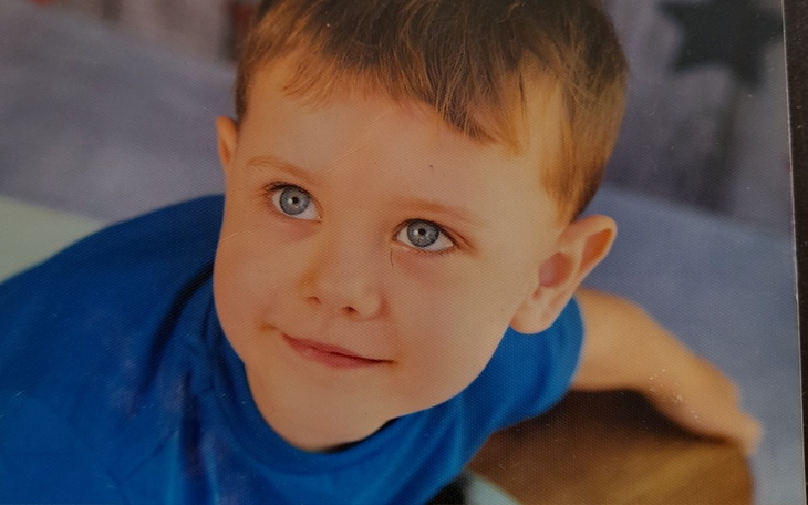 Chłopiec z niebieskimi oczami, uśmiechający się do kamery.