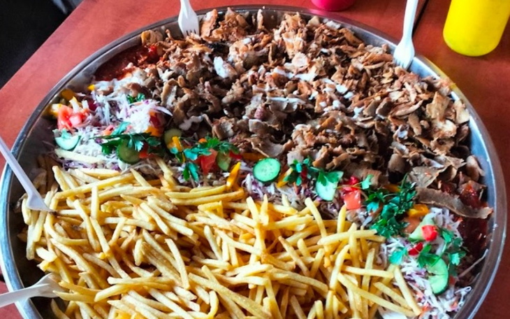 Duża taca z jedzeniem, w tym frytkami i mięsem, podana w restauracji.