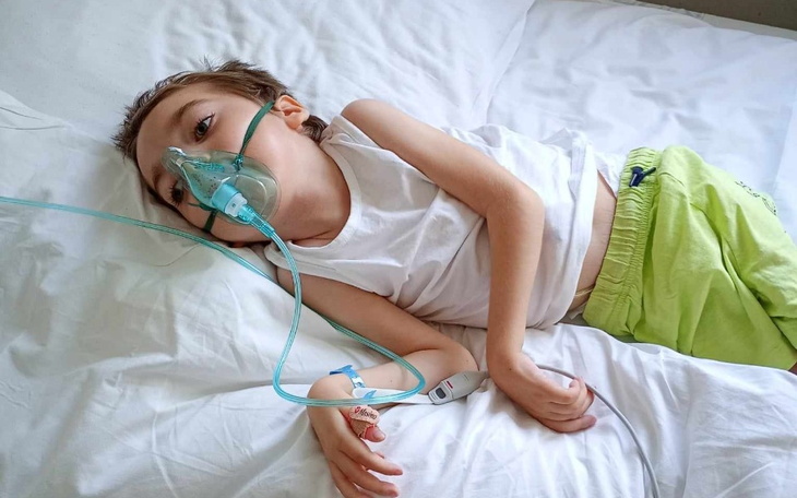 Chłopiec leżący na łóżku z maską tlenową, potrzebujący wsparcia zdrowotnego.