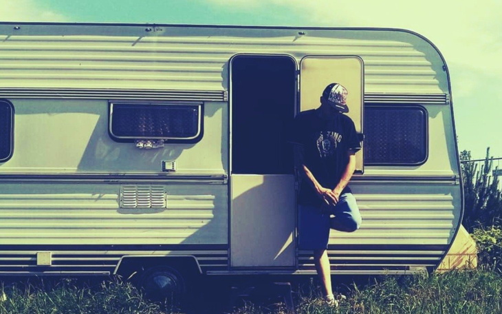 Mężczyzna stoi w drzwiach przyczepy kempingowej na tle zieleni.