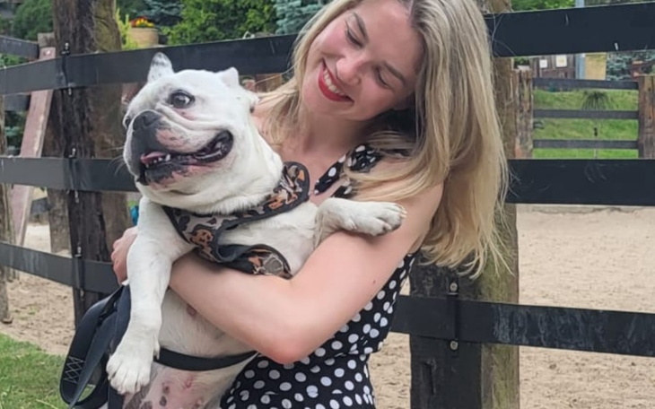 Kobieta trzyma psa w ramionach, uśmiechając się na tle ogrodu.