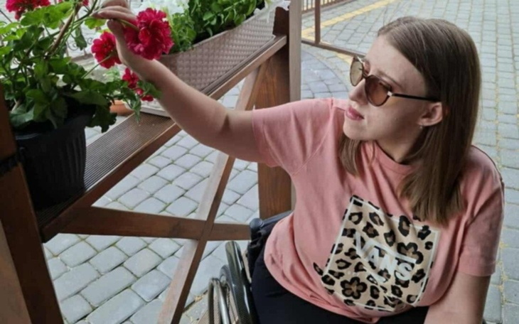 Kobieta w wózku inwalidzkim, dotykająca kwiatów.