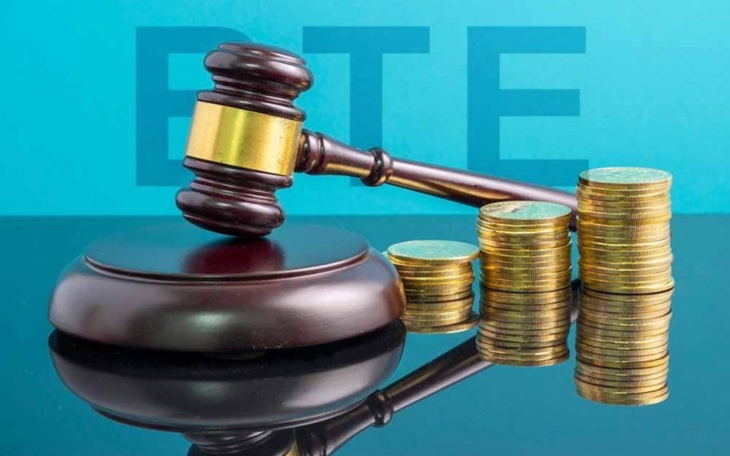 Młotek sędziowski obok stosu monet na tle niebieskim.