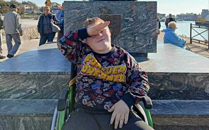 Chłopiec w wózku inwalidzkim, pozujący na tle pomnika.