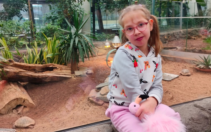 Dziewczynka w okularach, siedząca w ogrodzie z różowym pluszowym ptakiem.