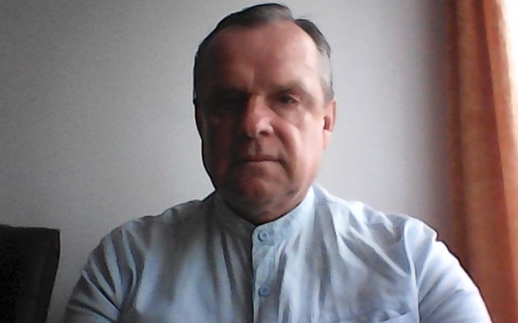 Mężczyzna w jasnej koszuli, siedzący w pokoju.