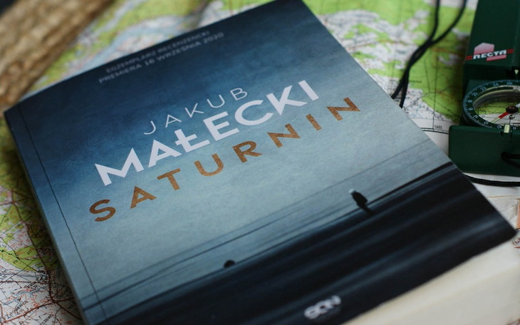 Książka 'Saturnin' Jakuba Małeckiego na tle mapy.
