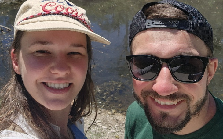 Młoda para uśmiechająca się do zdjęcia nad wodą w słoneczny dzień.