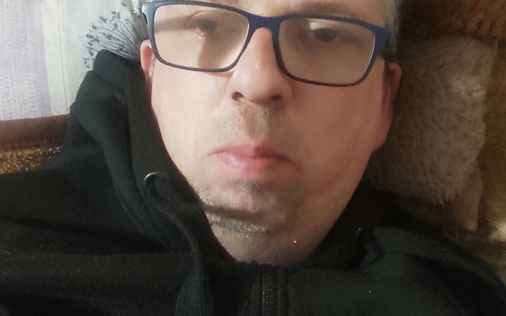 Portret osoby w czarnej bluzie, z wyraźnym wyrazem twarzy.