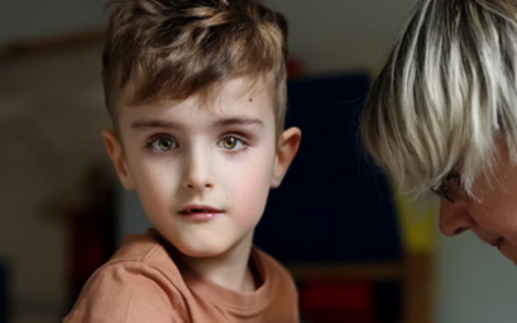 Chłopiec z ciekawym spojrzeniem, w tle dorosły.