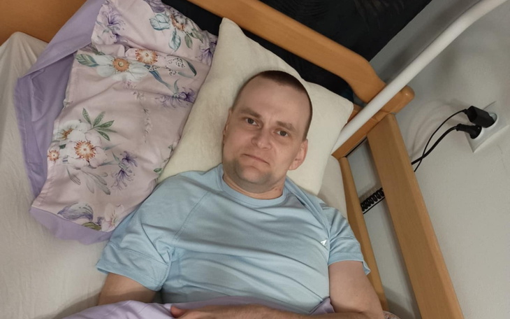 Mężczyzna leżący w łóżku, z uśmiechem na twarzy.