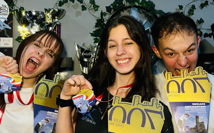 Trójka młodych ludzi z medalami, uśmiechają się i trzymają nagrody.