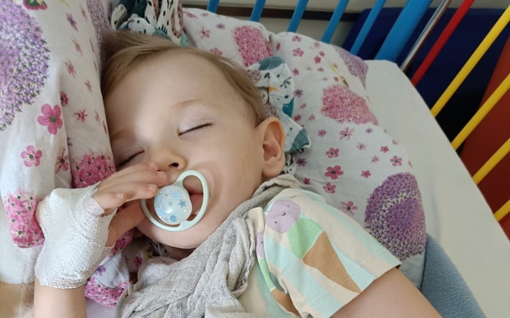 Małe dziecko śpiące w łóżku z smoczkiem w ustach.