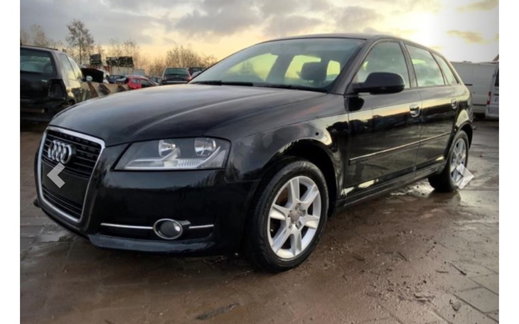 Czarny samochód marki Audi na placu z innymi pojazdami.