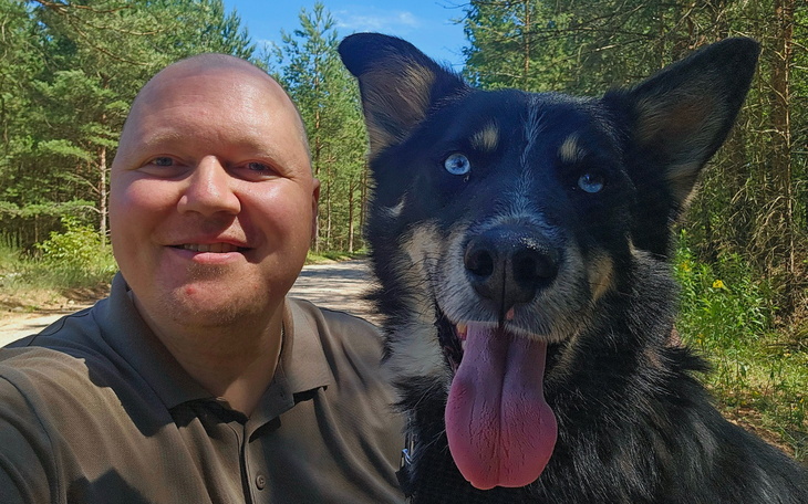 Mężczyzna z psem na leśnej drodze, uśmiechnięci i szczęśliwi.
