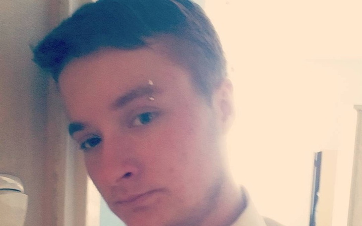 Młody mężczyzna z kolczykiem, patrzący w stronę obiektywu, w jasnym otoczeniu.