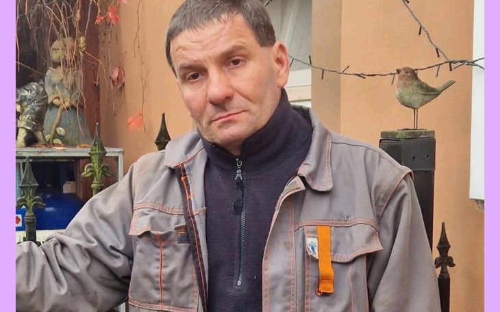 Mężczyzna w szarej kurtce, stojący przed domem.