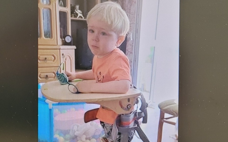 Mały chłopiec w nietypowym wózku, z zabawkami wokół.