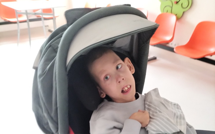 Chłopiec w wózku, z uśmiechem na twarzy, w jasnym otoczeniu.