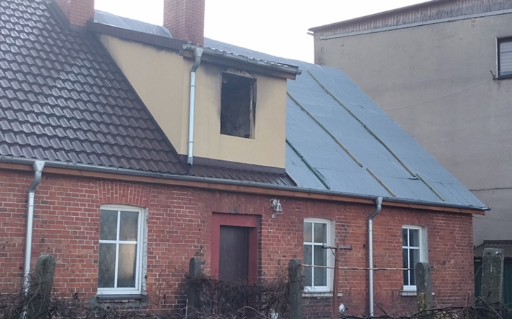 Zniszczony dom z brakującym oknem, widok na dach.