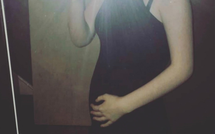 Kobieta w lustrze trzyma rękę na brzuchu.