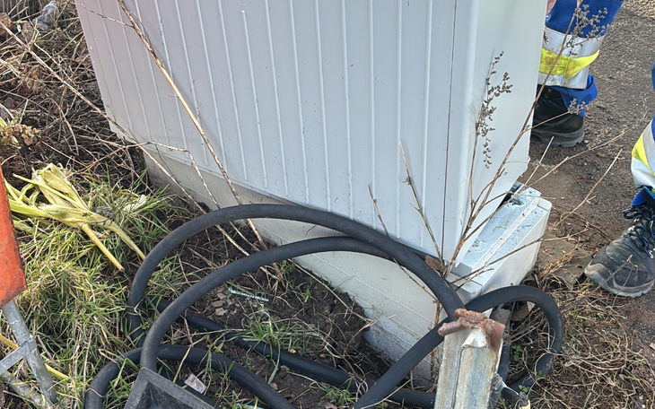 Zbliżenie na kabel i obiekt w terenie, z roślinnością w tle.